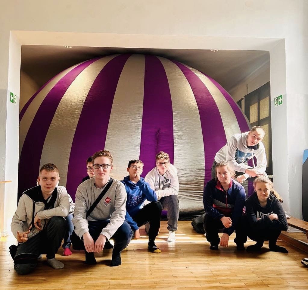 Przed dmuchanym balonem kuca grupa osob