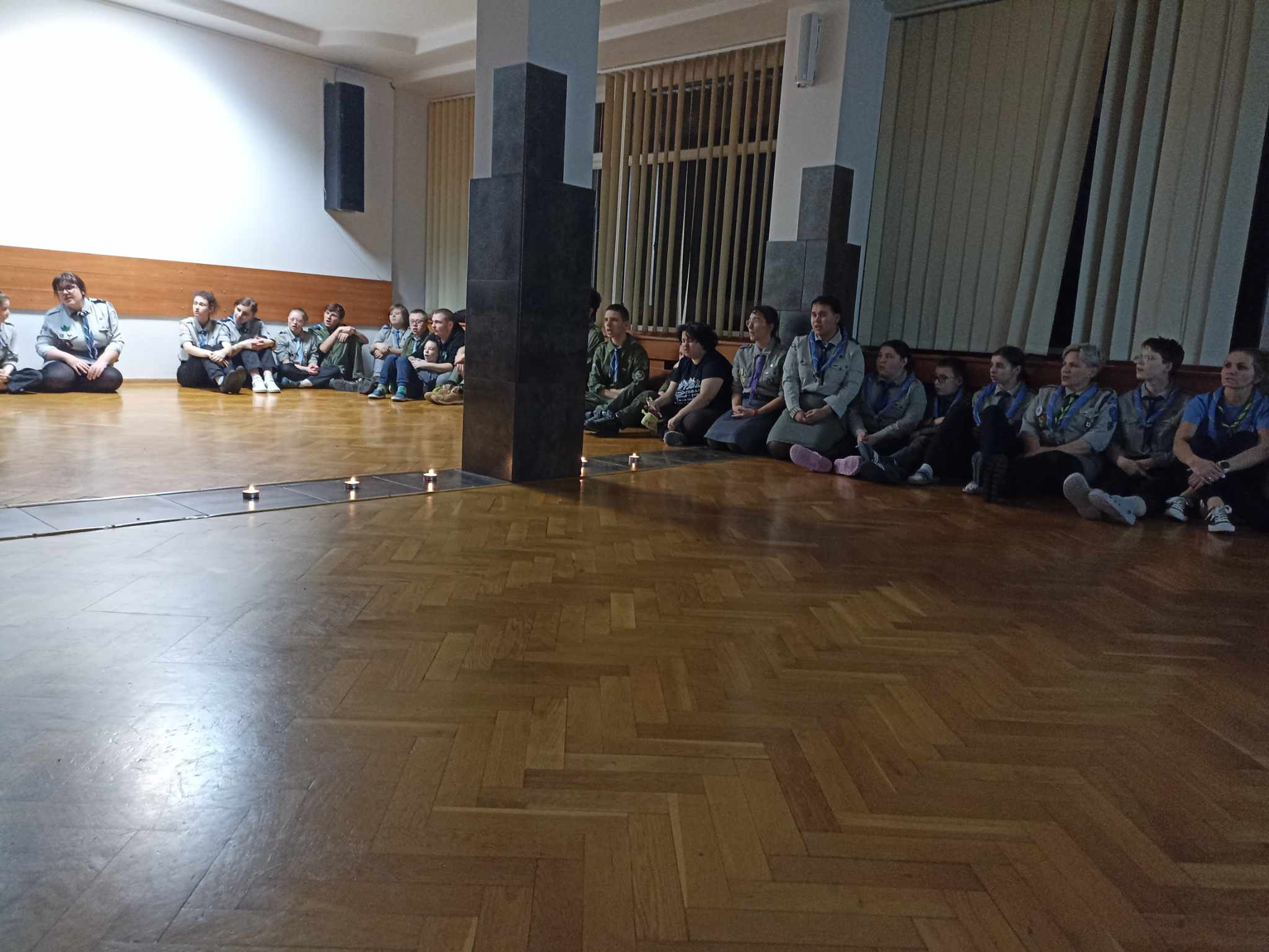 Na sali siedzi pod ścianą grupa osób