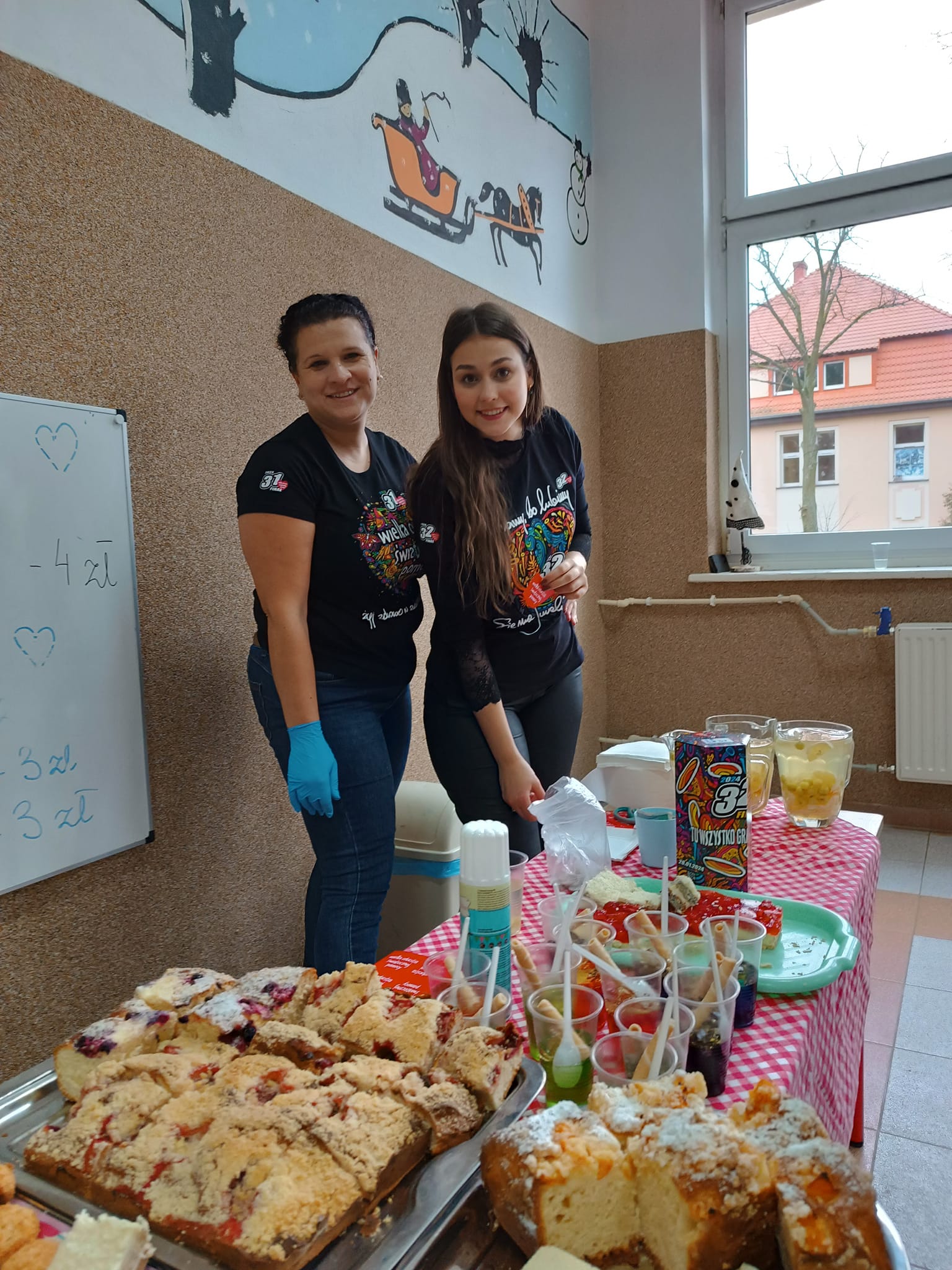 Za stolikiem z ciastami stoją dwie osoby 