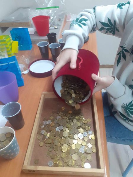 Do prostokatnego naczynia osoba wysypuje z wiaderka monety
