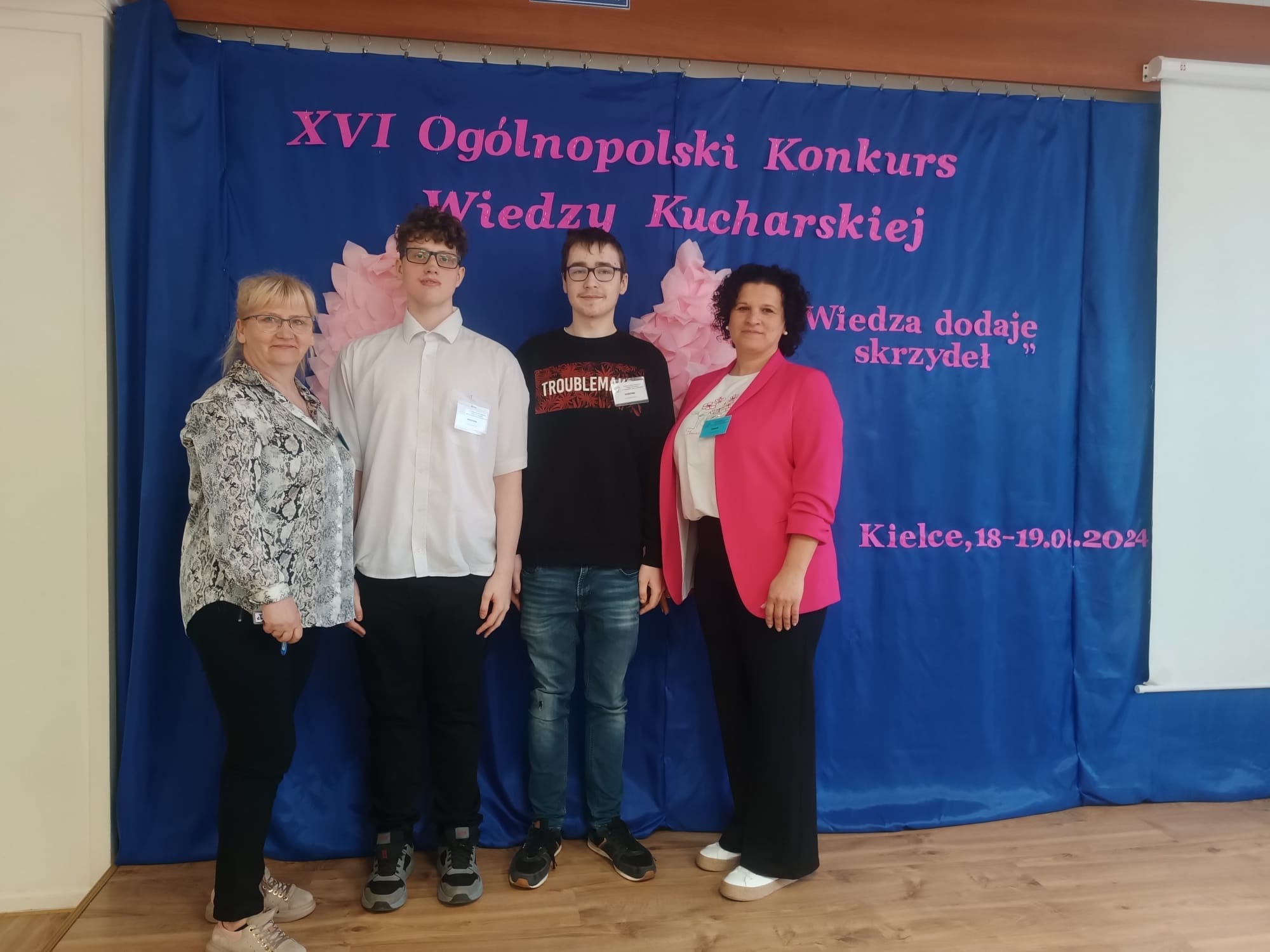 Grupa osób stoi pod ściana na tle napisów
