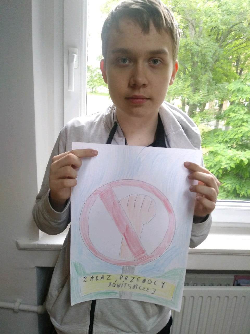 Osoba stoi przy oknie i trzyma w ręku kartkę 