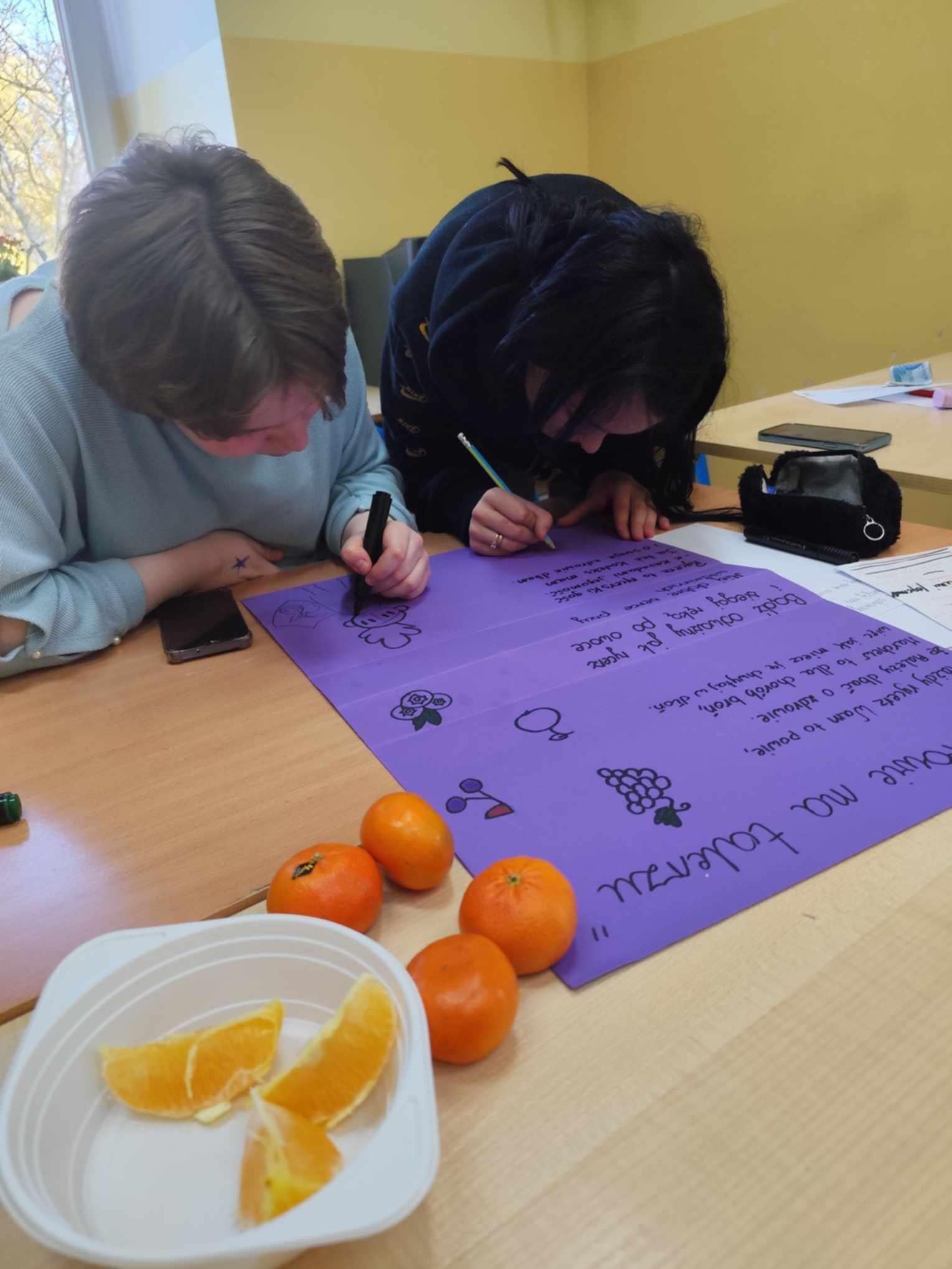 Na obrazku widać : 2 osoby, plakat, napisy, talerz z owocami.