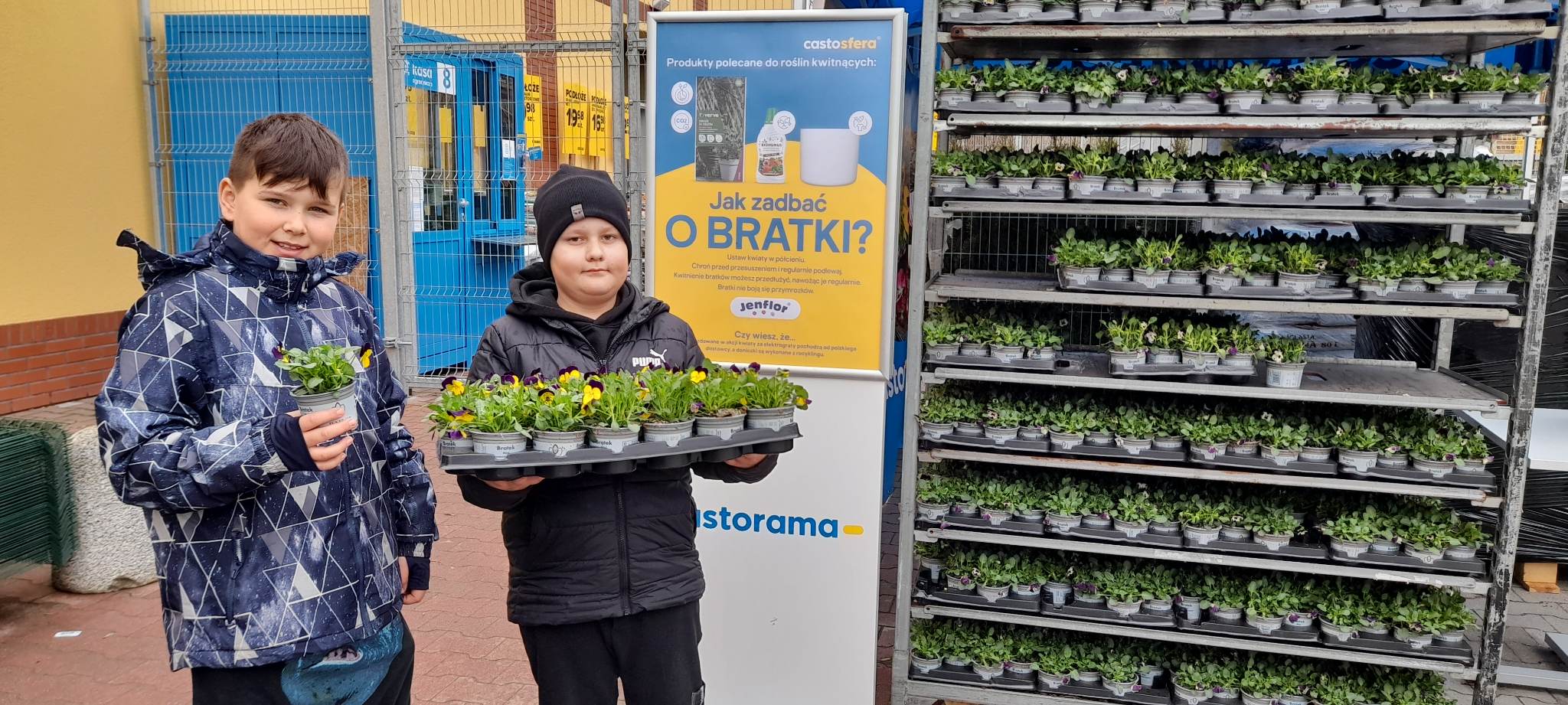 Po lewej stronie stoją dwie osoby. po prawej kwiaty. 