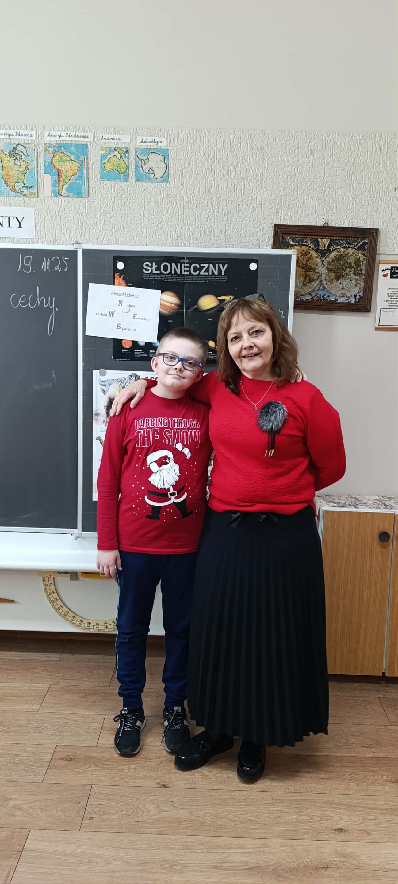 W pomieszczeniu znajdują się 2 osoby, tablica, sciana