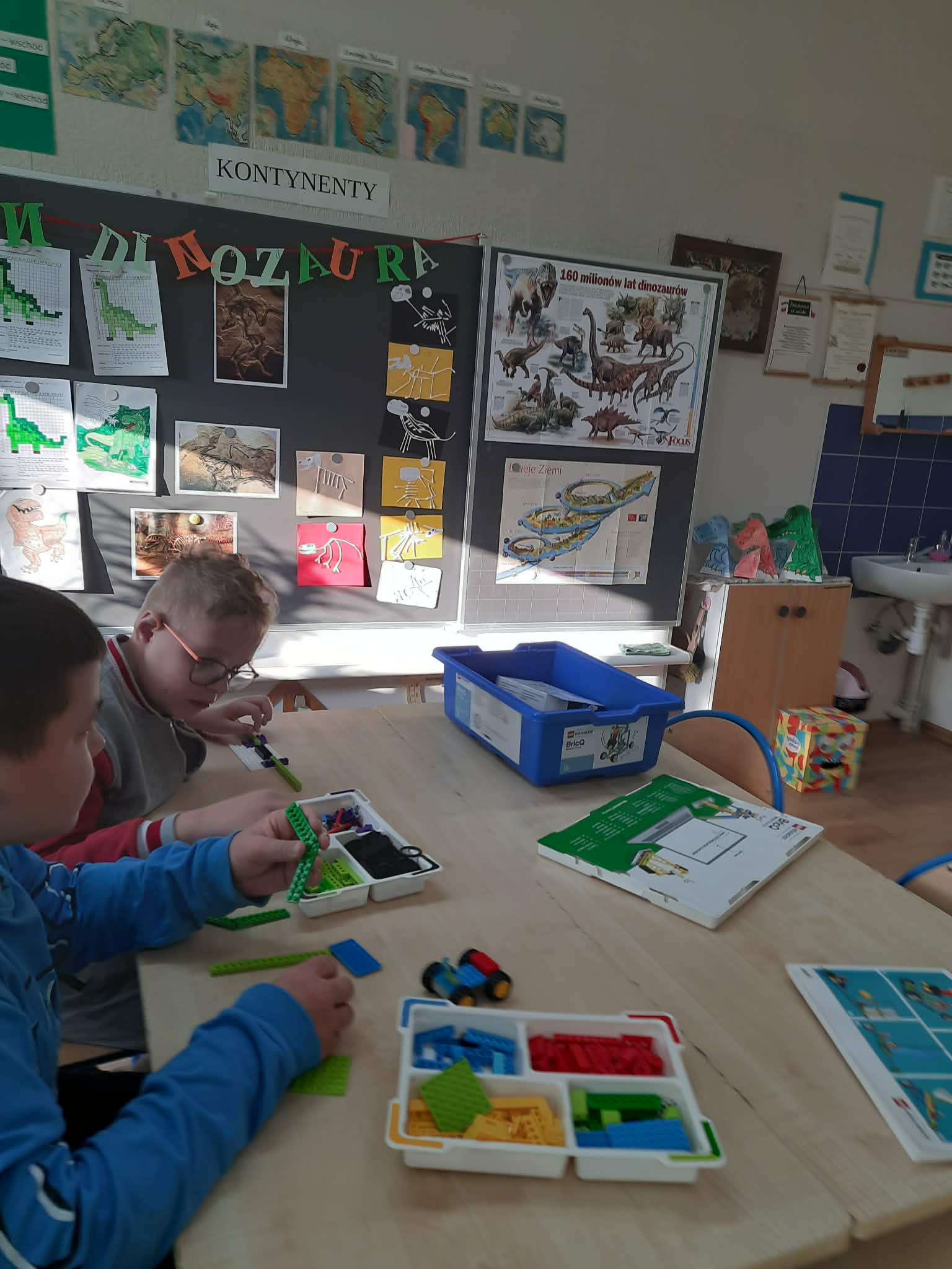 Na obrazku widać : 2 osoby , stol, klocki.