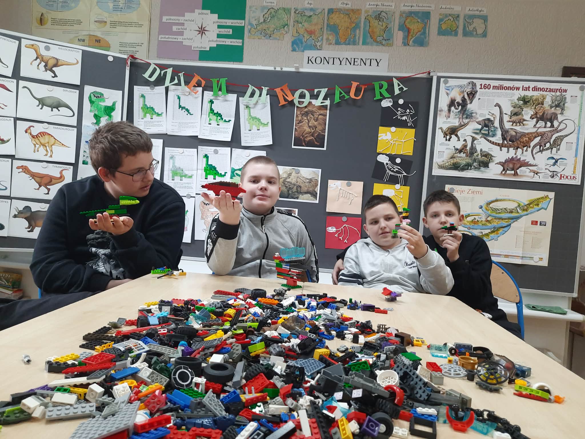 Na obrazku widać : 4 osoby , stol, klocki.