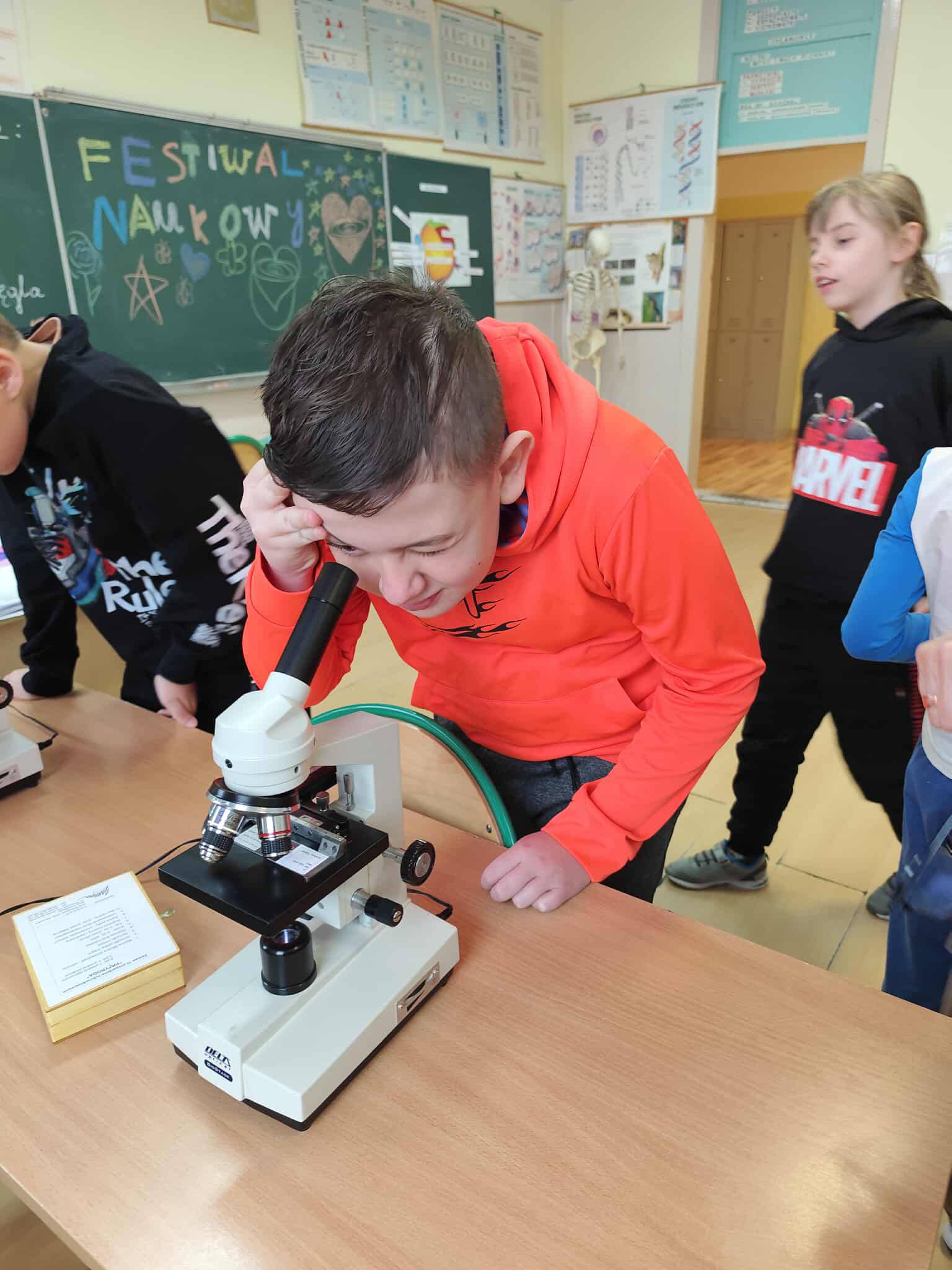 Na obrazku widać: grupę osób, mikroskop, tablicę 