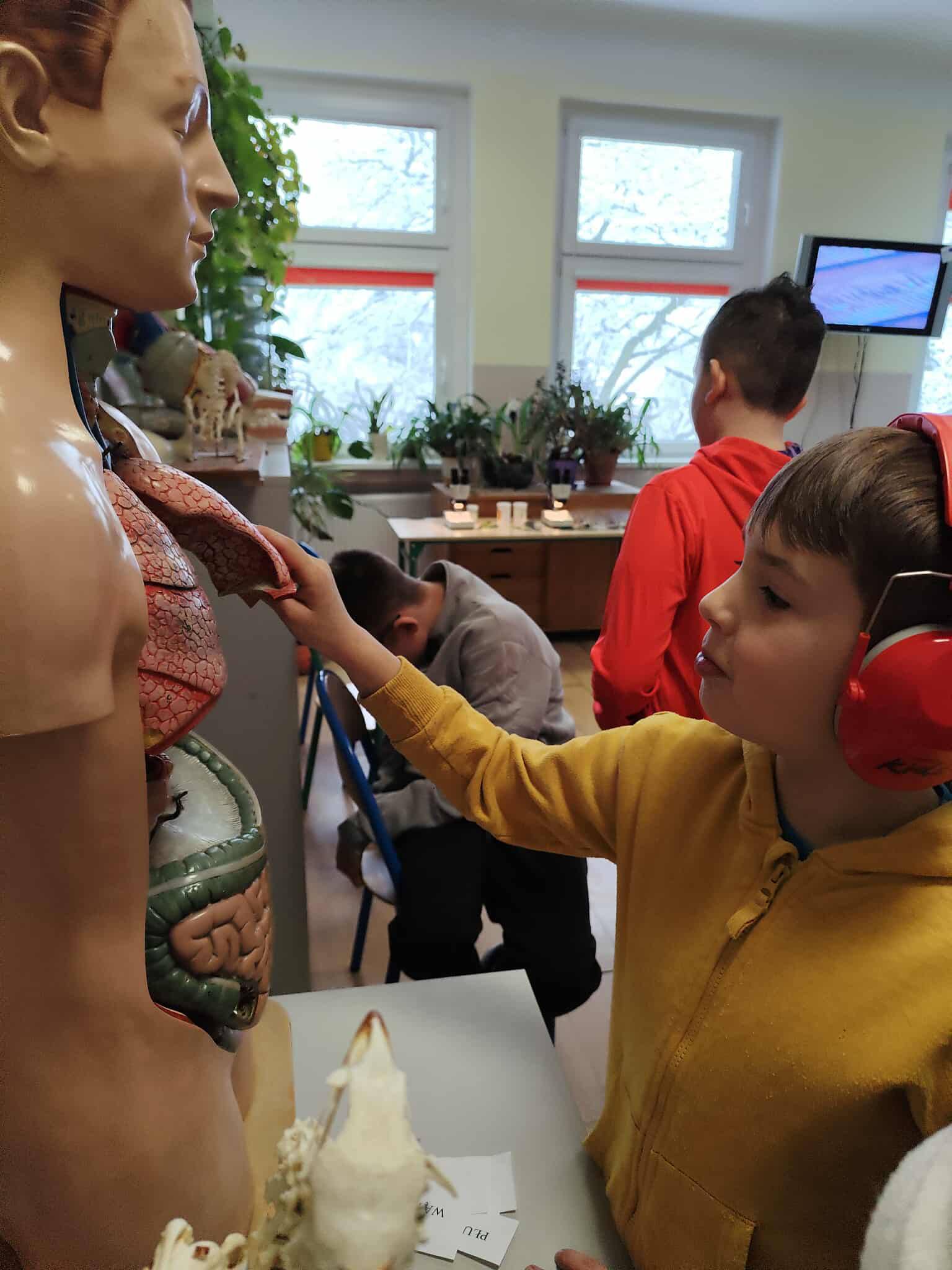 Na obrazku widać: grupę osób, okno, ekran telewizora, model