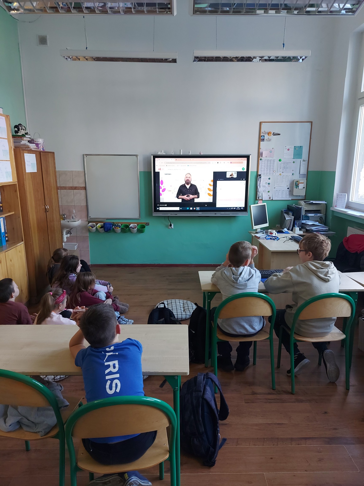 Na obrazku widać: grupę osób, krzesła, ekran 