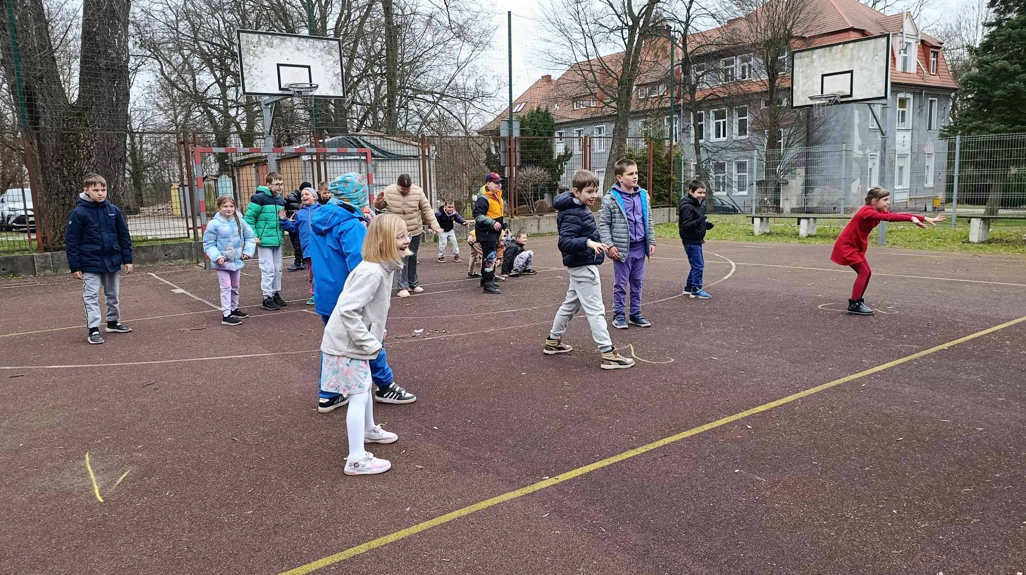 Na obrazku widać : grupę osób, drzewa, boisko. 